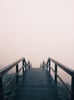 A wooden bridge descends into fog.