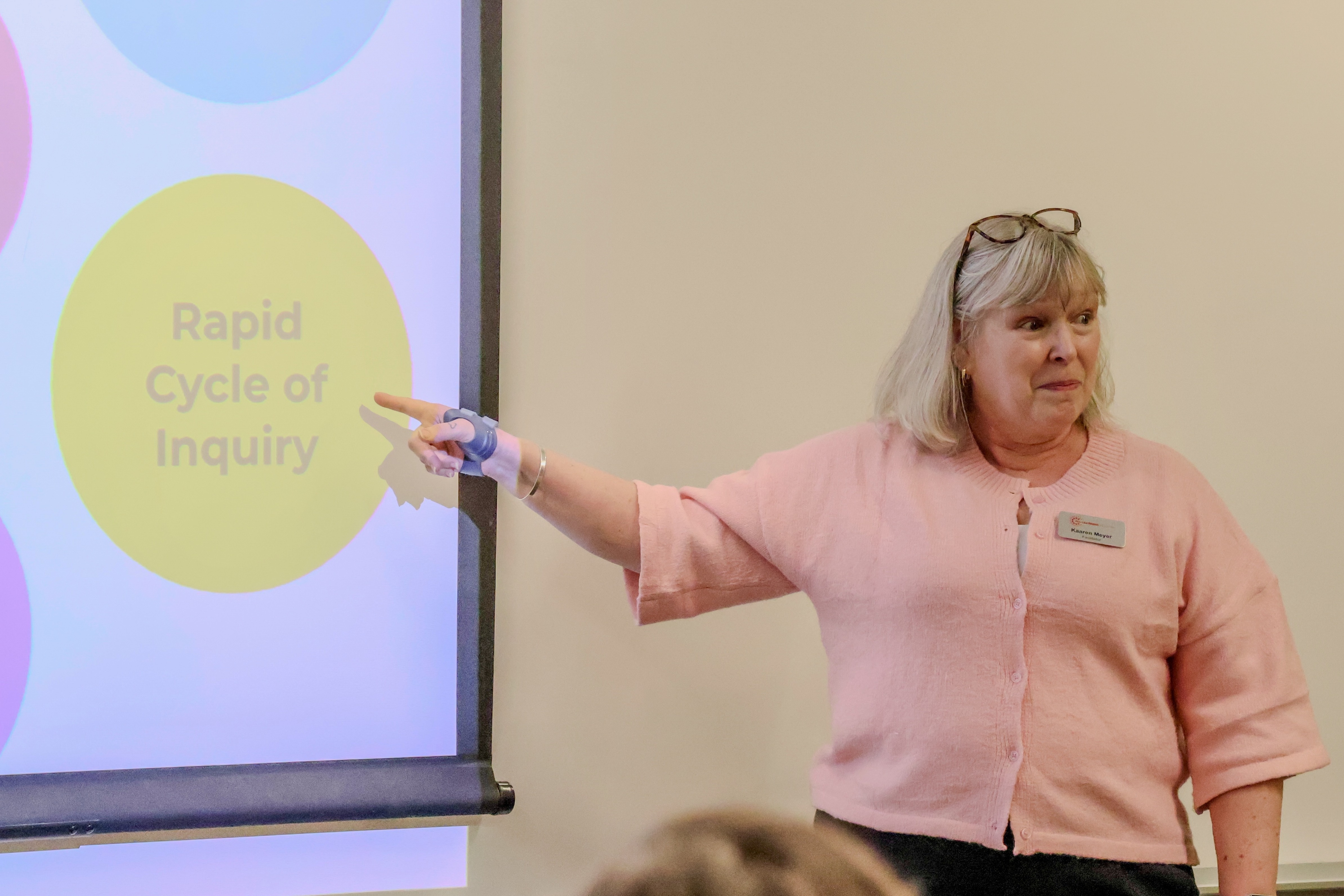 Kaaren Meyer speaking to a group of teachers. Kaaren is pointing to a screen that shows a yellow circle with the words 