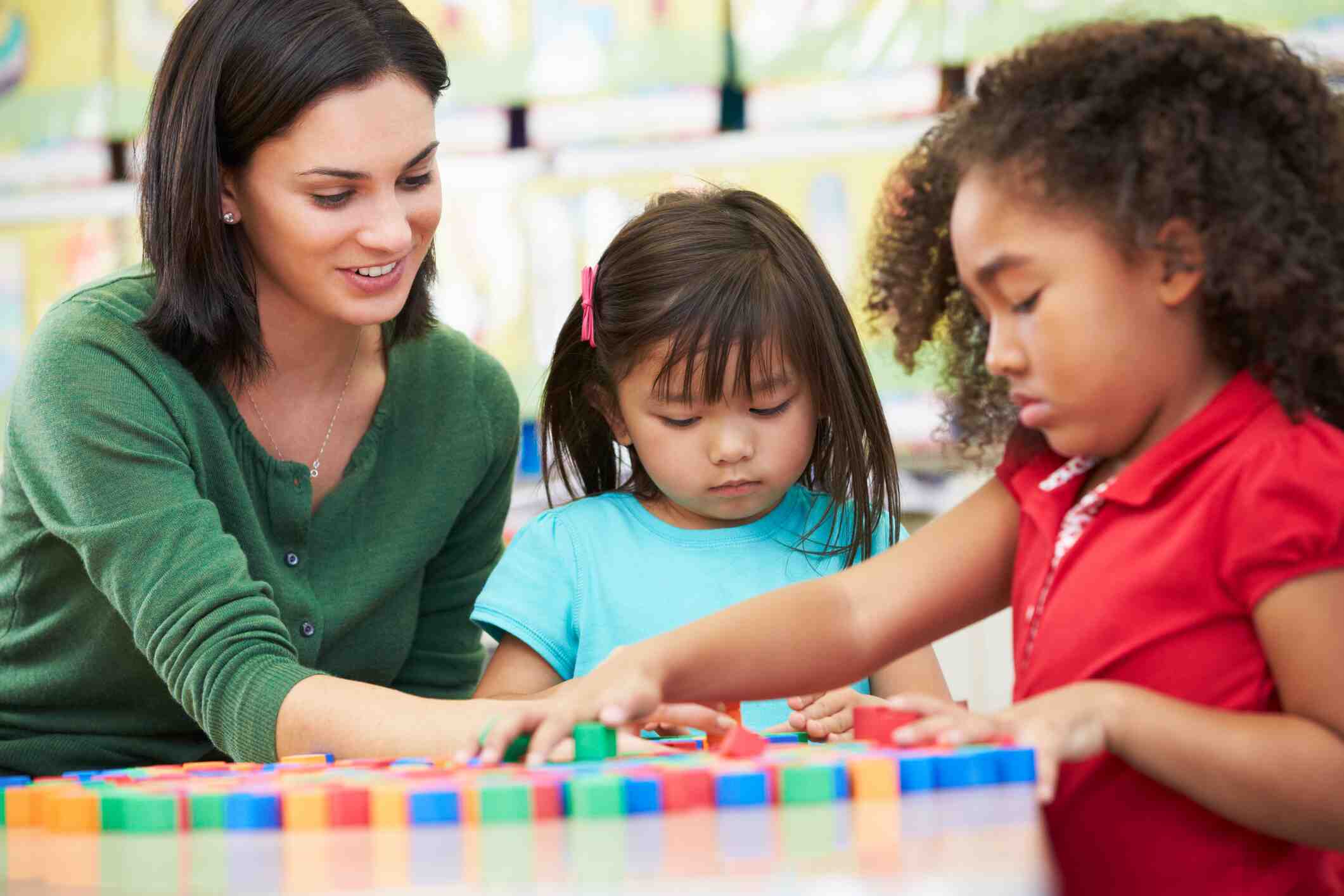 A female teacher looks on as early learners count with blocks.