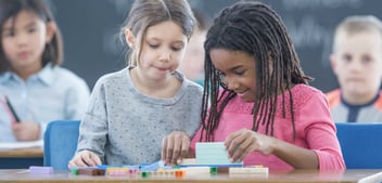 A young black girl shows her classmate how to work out a math problem.