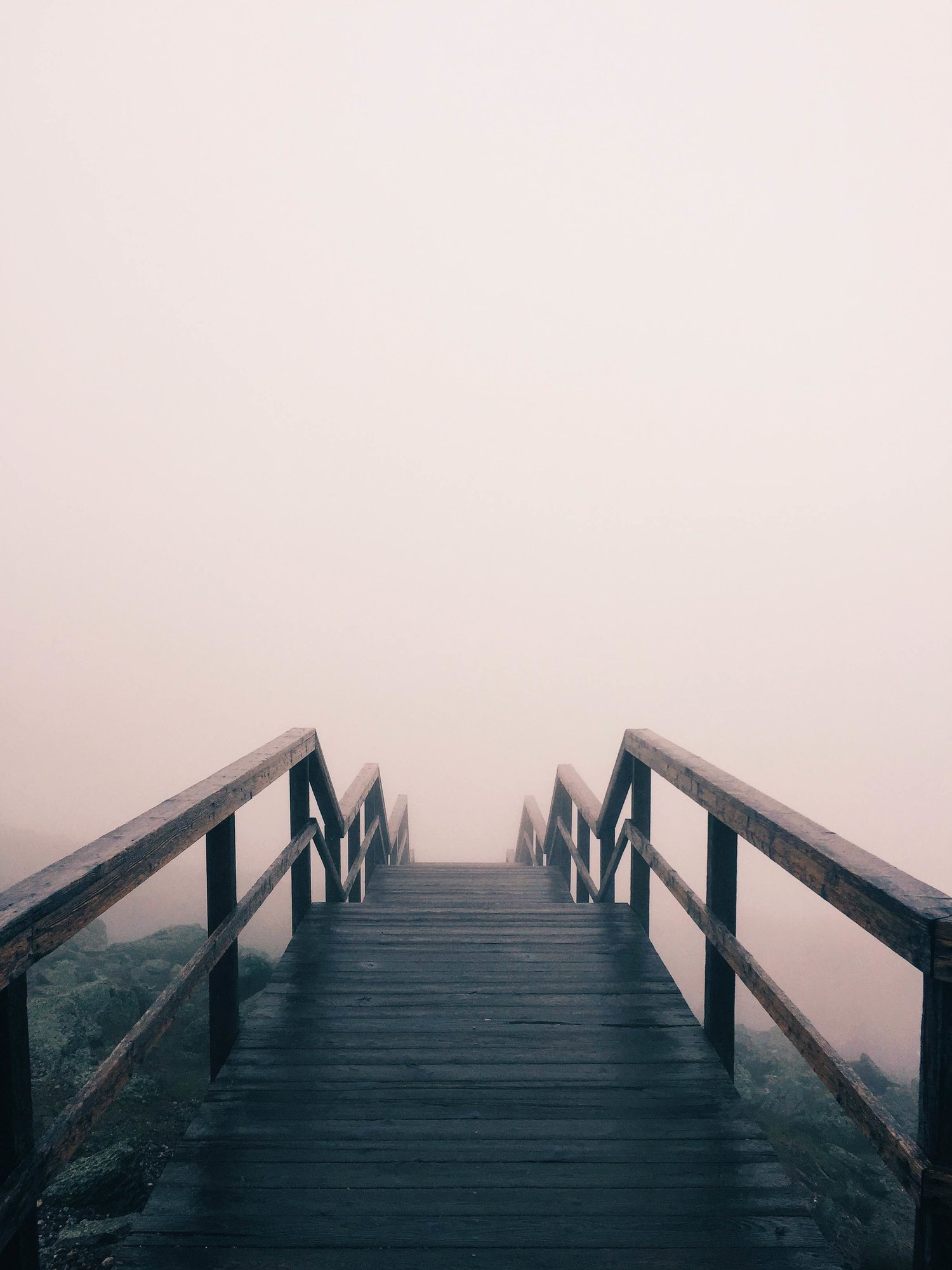 A wooden bridge descends into fog. 
