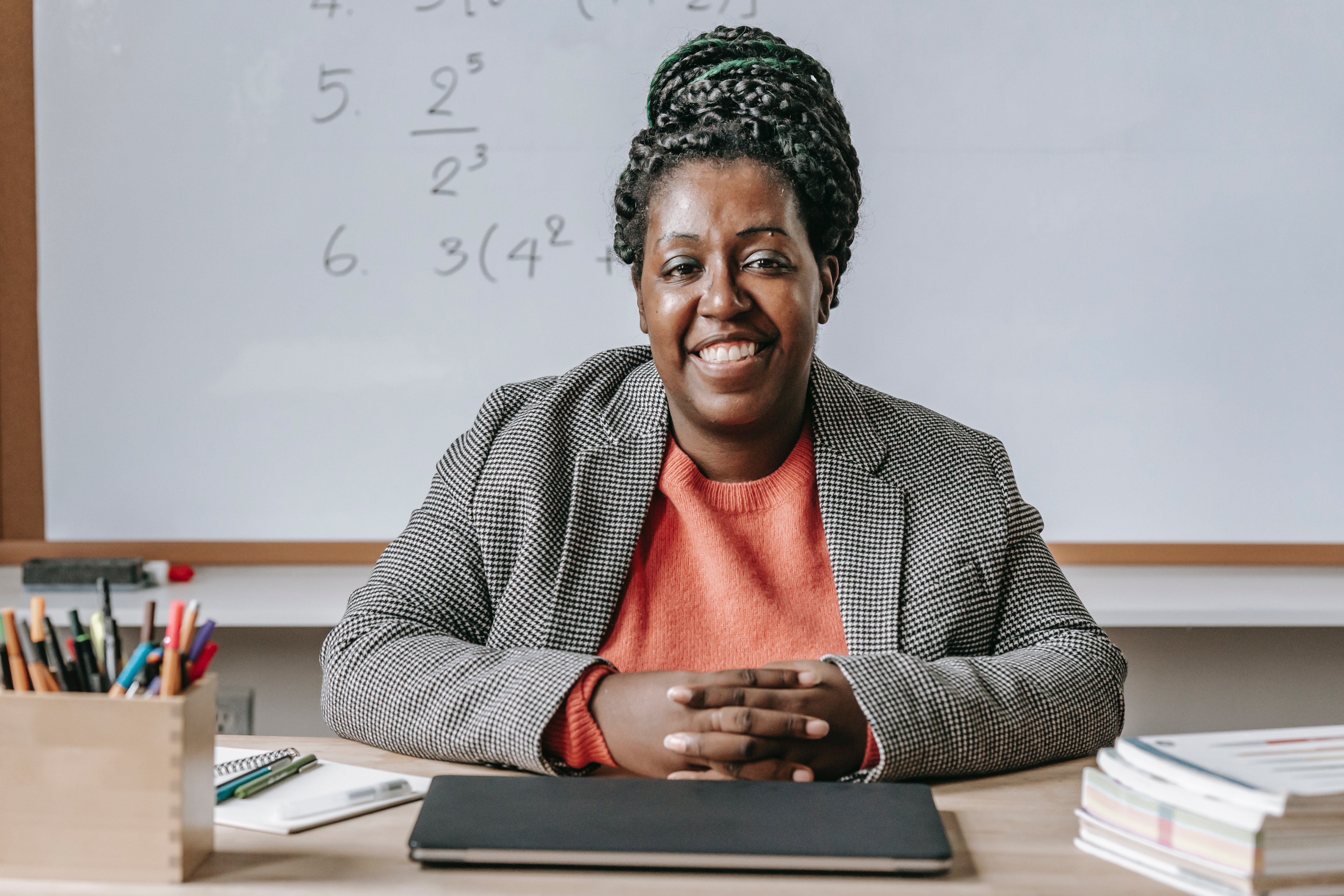 A black math teacher smiles in front of a whiteboard
