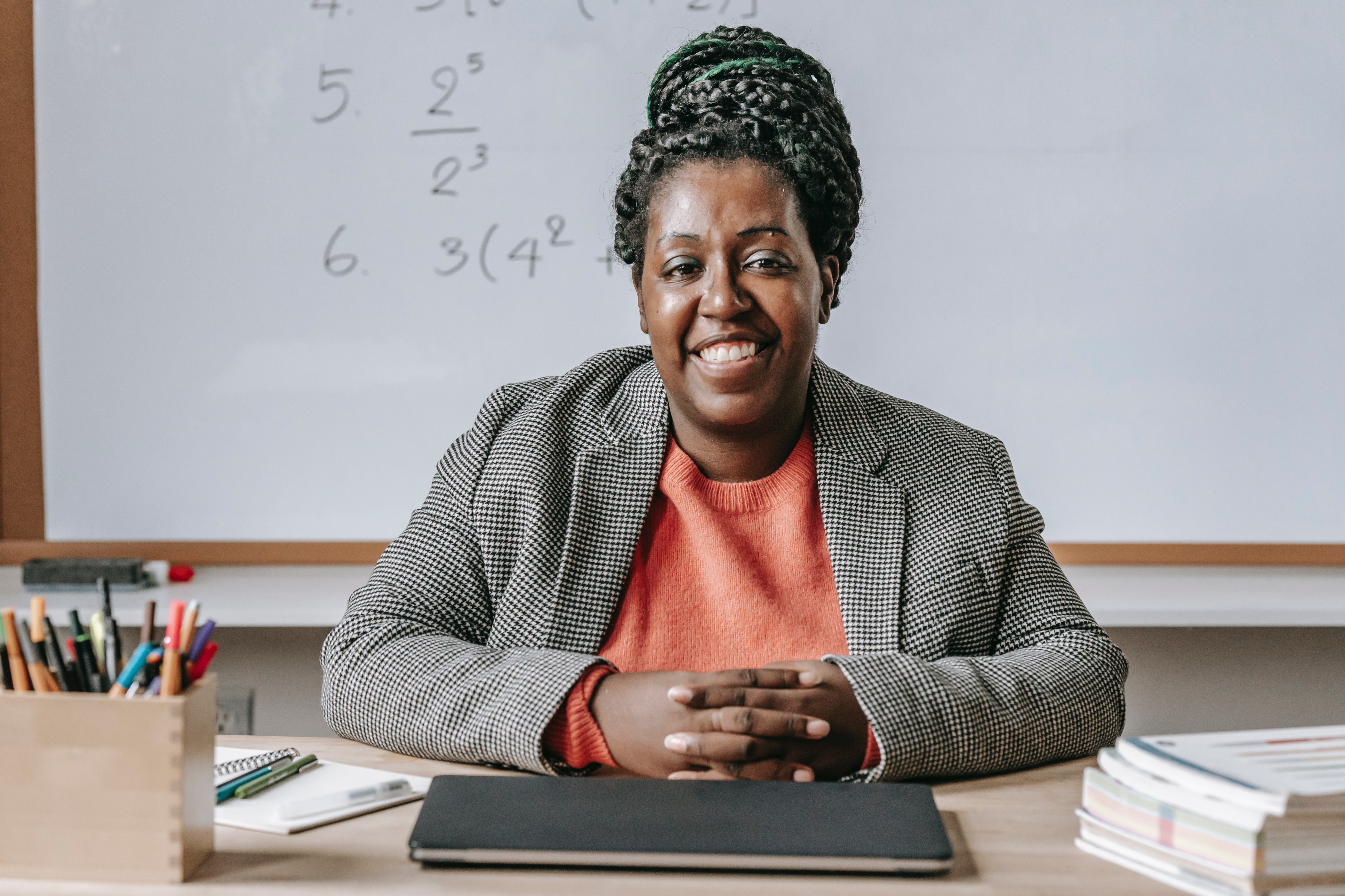 A black math teacher smiles in front of a whiteboard A black math teacher smiles in front of a whiteboard